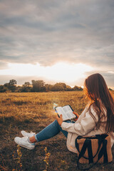 Christian woman holds bible in her hands. Reading the Holy Bible in a field during beautiful...