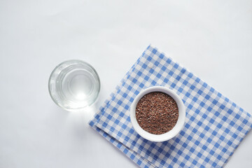 top view of flax seeds in a container and glass on water on table 