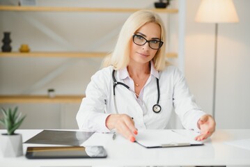 Portrait shot of middle aged female doctor sitting at desk and working in doctor office