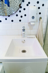 Fototapeta premium a white washbasin in the bathroom with a mirror and a soap dispenser on the wall