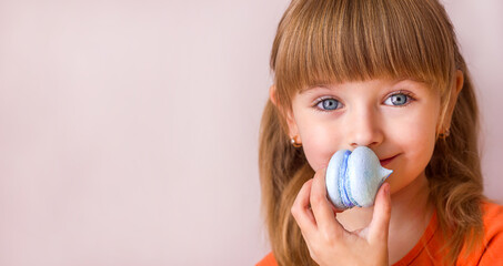 Beautiful little girl holding a blue sweet dessert macarons in her hands portrait close-up, sweet pastries happy childhood childish emotions, selective focus	