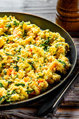 scrambled eggs with spinach and tomato in pan on wooden table background