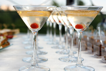 A row of glasses with champagne and cherries inside the glass are on the table.