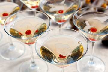 A row of glasses with champagne and cherries inside the glass are on the table.