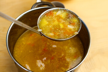 Freshly brewed soup in a saucepan is scooped up with a ladle for filling on plates.