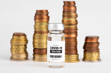 Vial glass bottle of COVID-19 vaccine standing next to money coin stack. SARS - CoV2 vaccination...