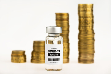 Vial glass bottle of COVID-19 vaccine standing next to money coin stack. SARS - CoV2 vaccination concept. Vaccine against coronavirus. Money behind a vaccine procurement. 