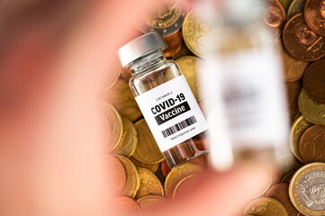 Vial glass bottle of COVID-19 vaccine standing on euro coins. SARS - CoV2 vaccination concept....