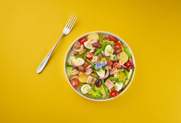 Fototapeta na wymiar Fresh salad of tuna, tomatoes, eggs, olives and green beans in a white bowl on yellow background. Salad Nicoise. French cuisine. Top view with copy space. Organic healthy food concept