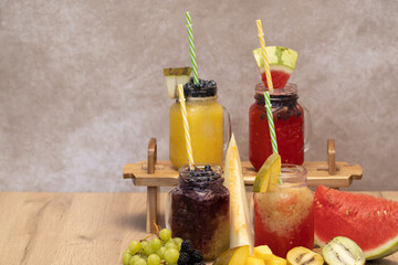 cold fruit juices or ice cream in glass jugs. four types of juices of different colours and flavours with straw surrounded by fruits such as watermelon, raspberry, kiwi, melon, with space for text.