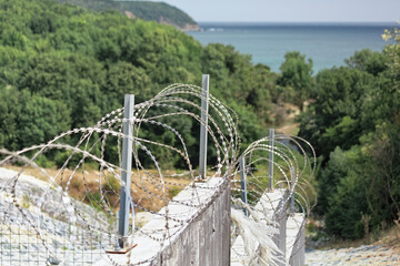 Barb wire and concrete walls with trees and sea in the background.