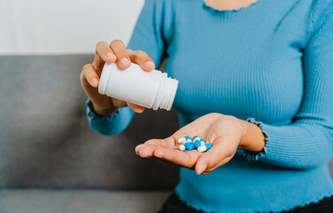 Young Pretty Asian woman holding medicine pills when sitting  on couch.