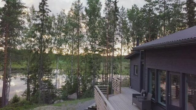 Woman on balcony enjoys lake and nature view at Nordic summer cabin, Aerial ascending over tree tops