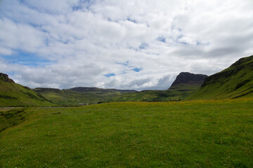 Wide angle views of Talisker Bay, Isle of Skye, Scotland, with its rocky beach, black stones, green fields, and a waterfall at the end of beach. Scattered clouds on blue sky, summer scottish weather.