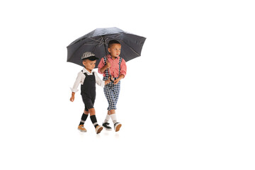 Portrait of two little boys, children in stylish vintage outfit walking under umbrella isolated over white studio background