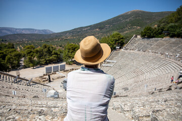 Tourist in Greece. A European woman from behind with a hat visits the theater of Epidaurus in the Peloponnese. Greece, July 2022.