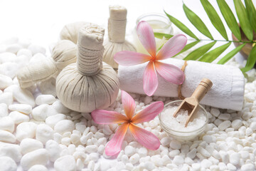 Obraz na płótnie Canvas Spa setting with frangipani ,bottles of essential oil , herbal ball, salt in bowl ,candle , herbal ,ball, leaves, on pile of white stones