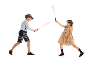 Two stylish children in vintage clothes playing badminton, having fun isolated over white studio background