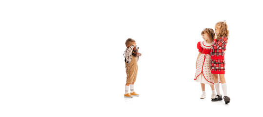 Portrait of little stylish children, boy taking photo with retro camera of two beautiful girls isolated over white studio background