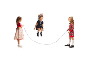 Portrait of little girls, children playing together, jumping over a rope isolated on white studio...