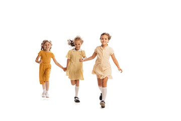 Naklejka premium Portrait of three little girls in yellow stylish dresses playing together isolated over white studio background. Cheerfully running