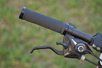 part of a black metal bicycle handlebar with a handbrake and a plastic handle on a background of...