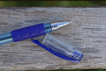 one blue white writing pen made of metal and plastic with a cap lies on a gray wooden table