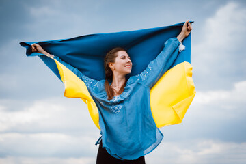 Happy free ukrainian woman with national flag on dramatic sky background. Portrait of lady in blue...