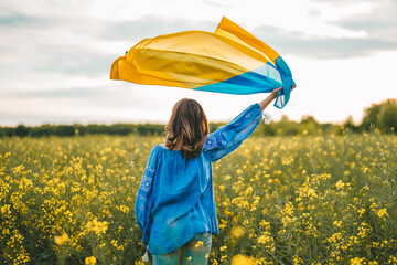 Ukrainian patriot woman waving national flag in canola yellow field. Rare, back view. Ukraine unbreakable, peace, independence, freedom, victory in war.