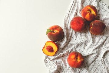Ripe peaches whole and halved on white checkered fabric on white background