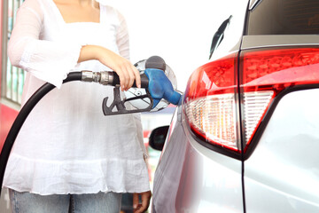 Blue fuel petrol pump nozzle against refueling auto car with petrol with female traveler holding...