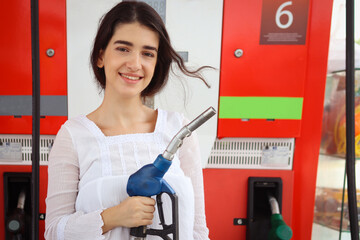 Portrait of happy smiling customer woman holding fuel petrol pump nozzle against for filling up her...