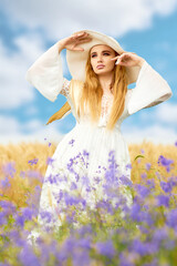 Fototapeta na wymiar Blonde girl in a wheat field in a white dress and a straw hat in summer