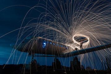 Rotating burning steel wool,Long exposure night shooting,Steel wool fireworks,Fire show,Night scenery with lighting effects,Sparks from metal. Old plane on the hill.