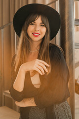  Close up autumn I portrait of elegant woman in black hat and blouse posing in bohemian interior with stairs.