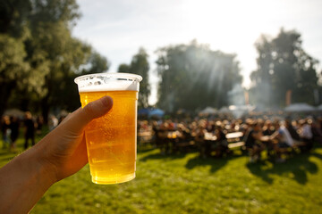 A plastic glass of beer in hand. Outdoor summer festival.