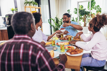 A multi-generational African-American family enjoying food at their dinner table.