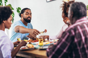 A multi-generational African-American family enjoying food at their dinner table.