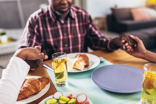 A Multi-generational African-American Family Saying Grace At Dinner Table And Holding Hands