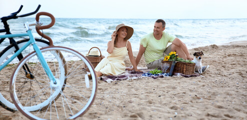 Mature couple with cute dog having picnic on sea beach