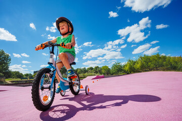 Small boy learn to ride bicycle with learning wheels, low angle
