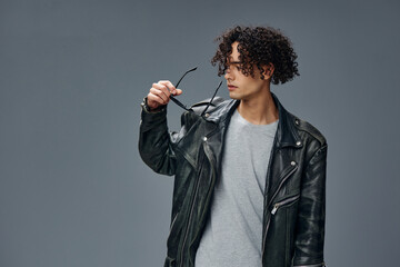 Stylish tanned curly man leather jacket in mirror trendy sunglasses posing isolated on over gray studio background. Cool fashion offer. Huge Seasonal Sale New Collection concept. Copy space for ad