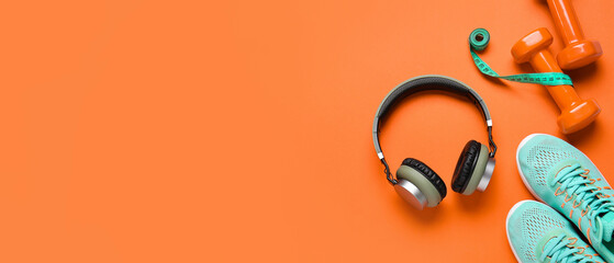 Sports shoes with headphones, measuring tape and dumbbells on orange background with space for text