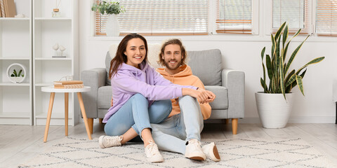 Happy young couple sitting on soft carpet at home - Powered by Adobe