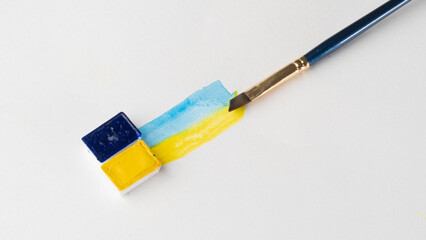 Cuvettes with blue and yellow paint with strips of paint and a brush on a white background place for inscription