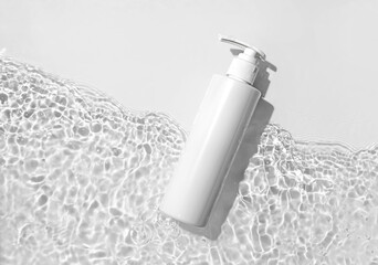 White cosmetic bottle on the water surface. Blank label for branding mock-up. Summer water pool fresh concept. Flat lay, top view.