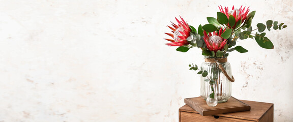 Vase with bouquet of protea flower on table near light wall in room