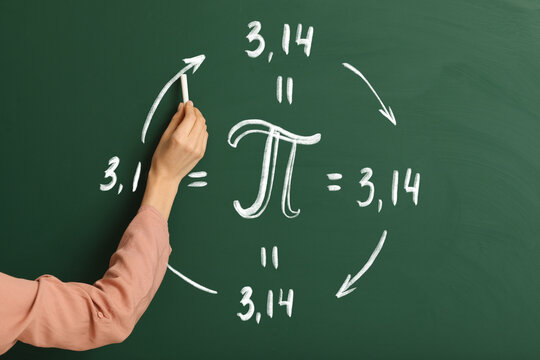 Female Teacher Writing Number Pi On Blackboard In Classroom