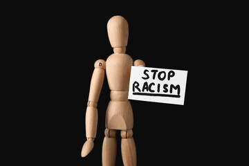 Wooden mannequin and paper sheet with text STOP RACISM on dark background