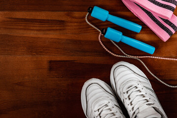 White sneakers, blue skipping rope and pink fitness elastic band on wooden background.